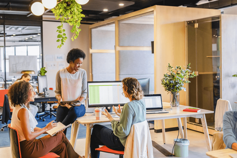 Diverse female colleagues in discussion using tablet in casual office meeting